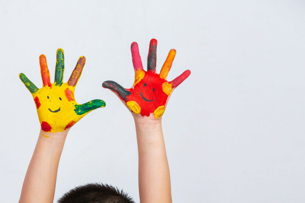 Criança com as mãos pintadas com carinhas coloridas