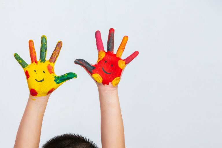 Criança com as mãos pintadas com carinhas coloridas